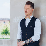 tattooed man in white shirt and vest wearing a wooden bow tie